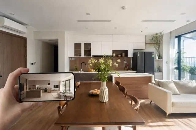 Căn hộ không gian mở phòng khách liền bếp với sofa, bàn ăn và tủ bếp sáng màu, điện thoại hiển thị phối cảnh AI